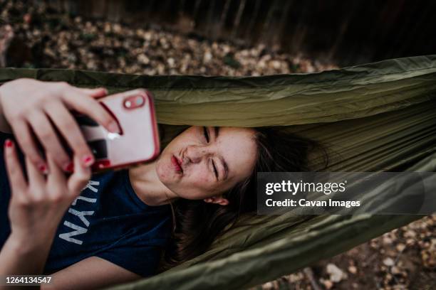 teen girl laying in hammock making silly faces into phone - hammock camping stock pictures, royalty-free photos & images