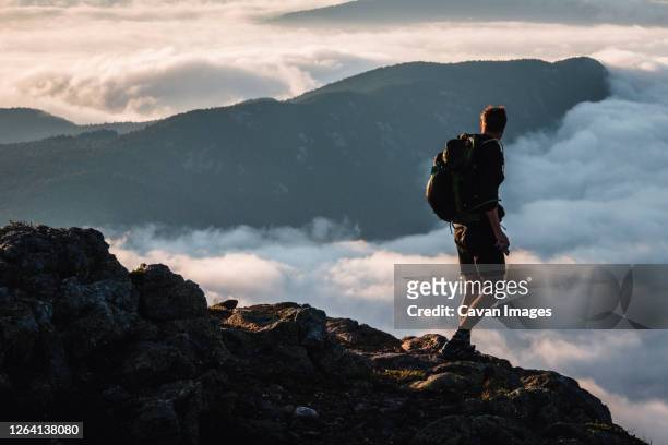 male hiker on summit gazes at mountain rising above clouds, maine - appalachian trail fotografías e imágenes de stock