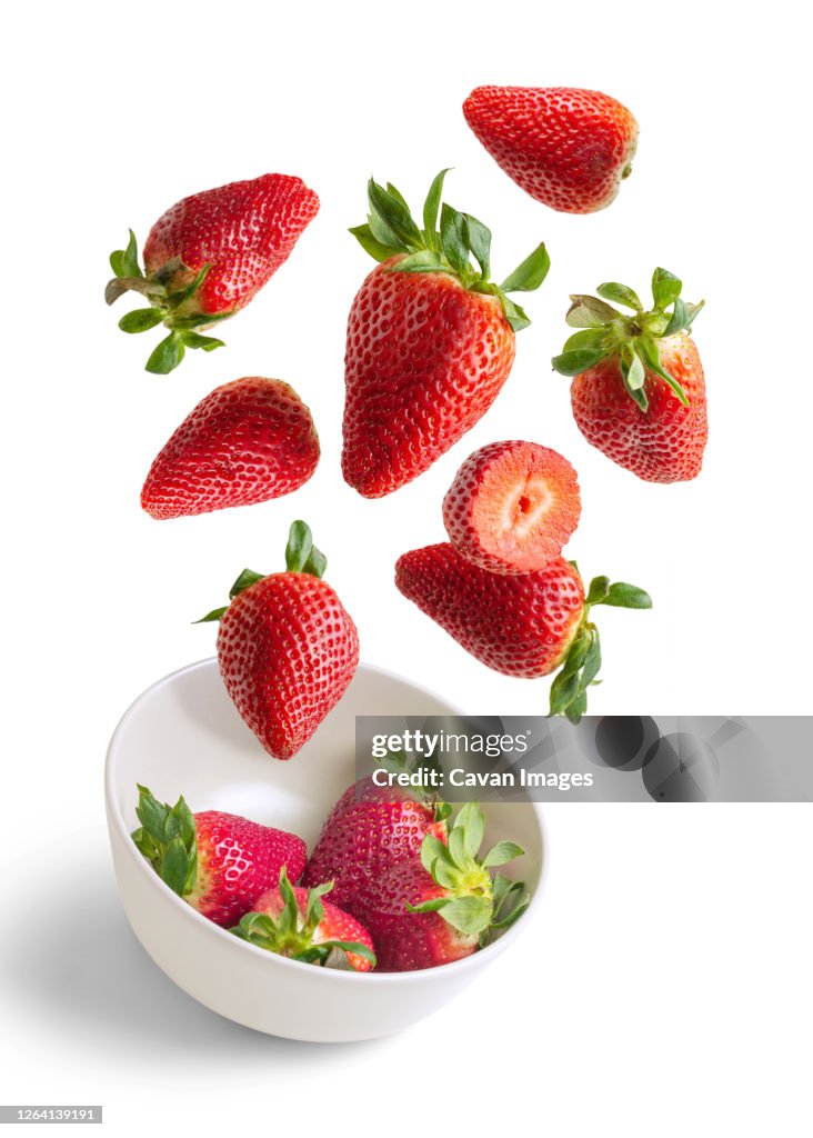 Strawberries flying in white bowl isolated from the background