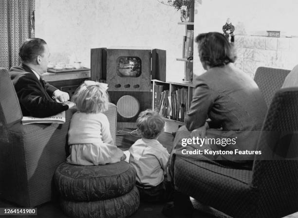 Rear view of a traditional family group all facing a television set in a living room, 1950.