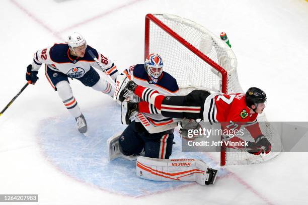 Kirby Dach of the Chicago Blackhawks gets tripped up against Mikko Koskinen and Caleb Jones of the Edmonton Oilers during the second period in Game...