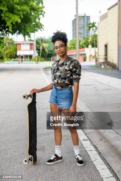 verticale d’une adolescente afro-américaine avec son skateboard extérieur sur une rue résidentielle à miami - short hair photos et images de collection