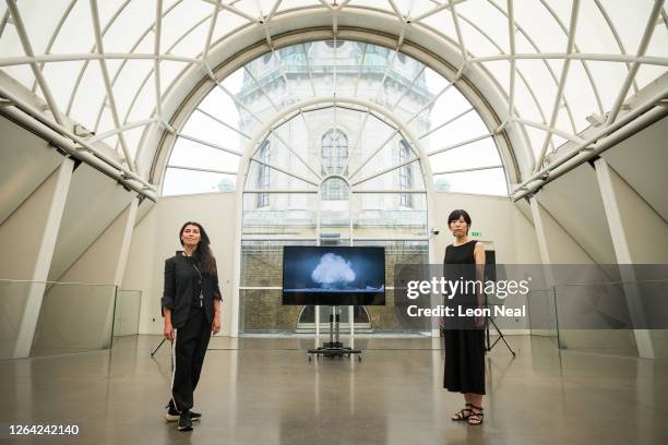 Artists Es Devlin and Machiko Weston pose for photographs while a screen displays a part of their commissioned video installation "I Saw The World...
