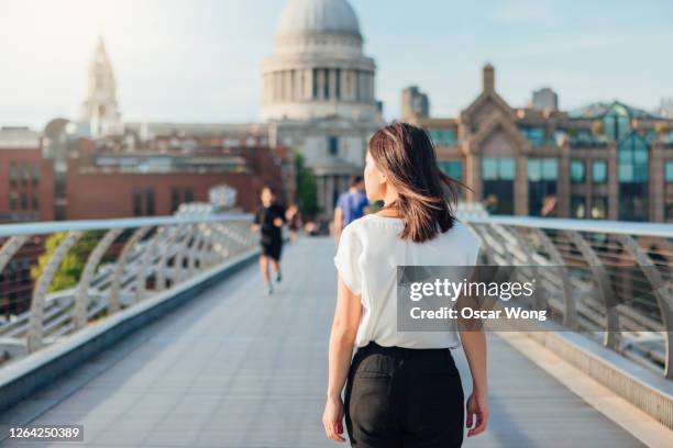 rear view of young businesswoman walking on footbridge in the city - chinese woman outside walking stock-fotos und bilder