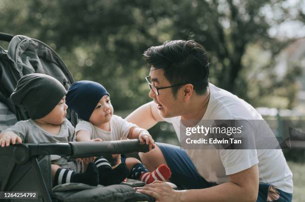 一個亞洲的中國年輕家庭在週末與雙胞胎男嬰在公共公園有結合時間。 - asian twins 個照片及圖片檔