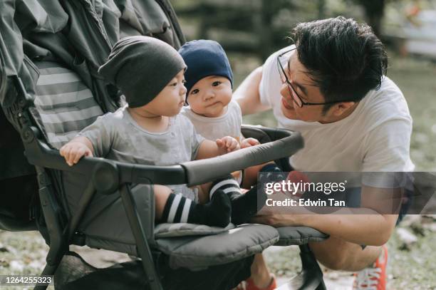 une jeune famille chinoise asiatique ayant le temps de liaison pendant le week-end au parc public avec leurs garçons jumeaux de bébé - asian twins photos et images de collection