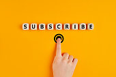Male hand pressing subscription button with the word subscribe written on wooden blocks. Concept of online registration.