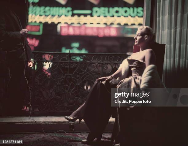 American actress Barbara Payton posed seated in a chair next to an open window and balcony in October 1952.