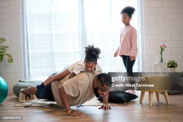 a african father doing push up exercise while giving his daughter playing piggyback ride. family having fun playing and home workout on weekend. - dad press ups kids stock pictures, royalty-free photos & images