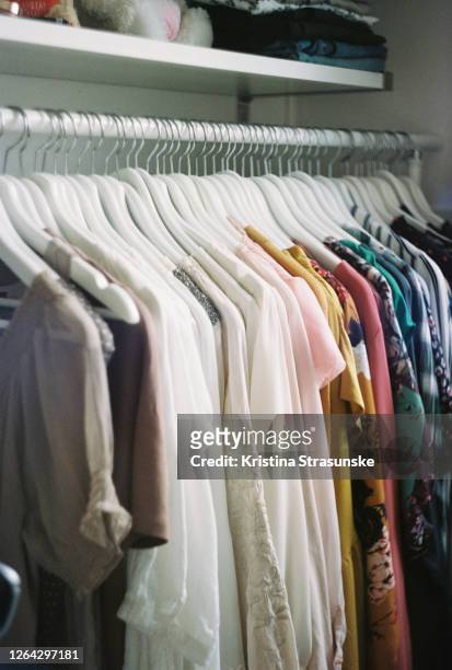 blouses in different colors hanging on a coathangers, arranged by color - armadio a muro foto e immagini stock