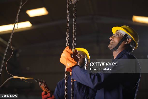 twee arbeiders die kettingtoestel bij fabriek in werking nemen - lier stockfoto's en -beelden