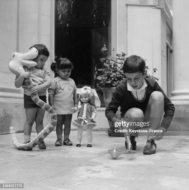 Trois enfants jouent avec des nouveaux jouets, un serpent en peluche, une poupée et une toupie, France en 1968.