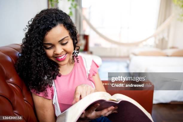 woman reading the bible and smiling on the sofa at home - evangelicalism stock pictures, royalty-free photos & images