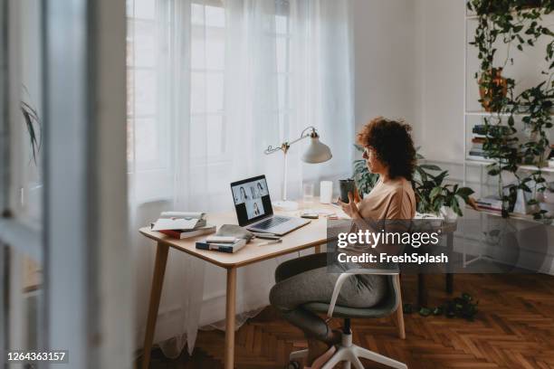 arbeiten von zu hause während der sperrung: eine glückliche frau, die an einem geschäftstreffen durch einen videoanruf auf ihrem laptop-computer teilnimmt - adapting stock-fotos und bilder