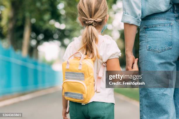 süße blonde mädchen trägt eine schutzmaske, die von ihrer mutter / einem babysitter zur schule gebracht wird - schulbeginn stock-fotos und bilder