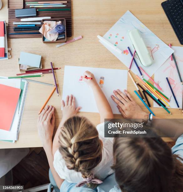 homeschooling: hands of an unrecognizable child drawing while sitting on her mother's lap, lockdown activities concept (overhead view) - babysitter stock pictures, royalty-free photos & images