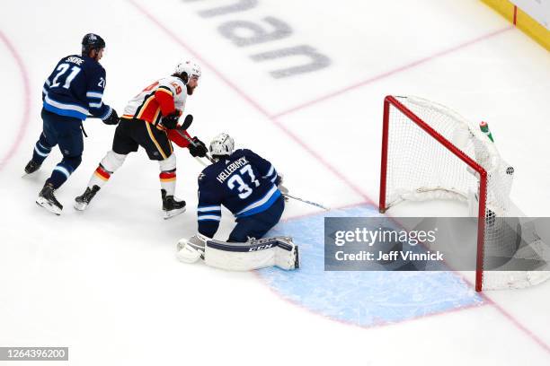 Dillon Dube of the Calgary Flames scores a goal on Connor Hellebuyck of the Winnipeg Jets during the first period in Game Four of the Western...