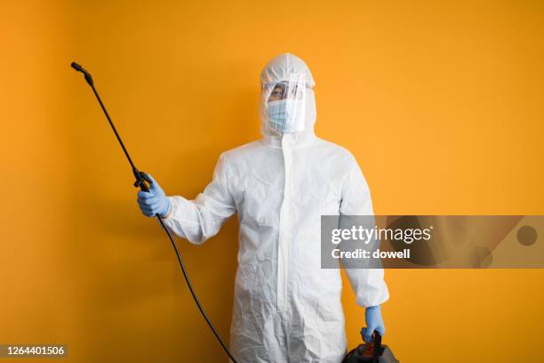 young man in protective suit disinfects on orange backgrounds - pest foto e immagini stock