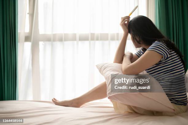 asian young woman looking at pregnancy test with disappointed expression - infertility stock pictures, royalty-free photos & images