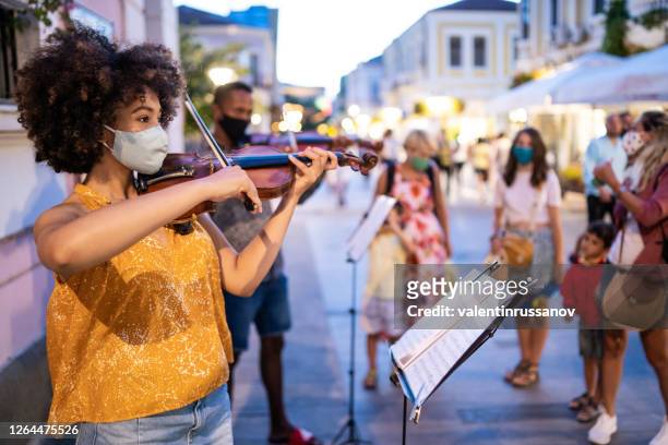 street afro musicians playing violin and wearing protective face mask, during covid-19 - masked musicians stock pictures, royalty-free photos & images