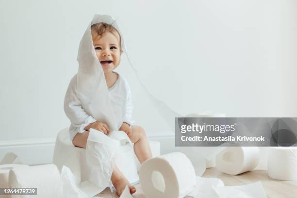 cute baby girl sitting on white chamber pot with toilet paper rolls. funny toddler sitting on potty chair and playing with toilet paper. - baby pee stockfoto's en -beelden