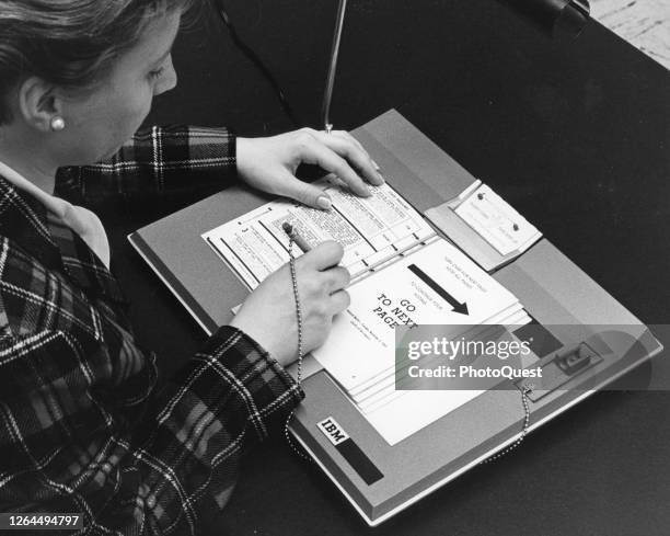 Over-the-shoulder view of an unidentified woman as she demonstrates how to use an IBM voting machine, 1966. The voter casts their ballot by punching...