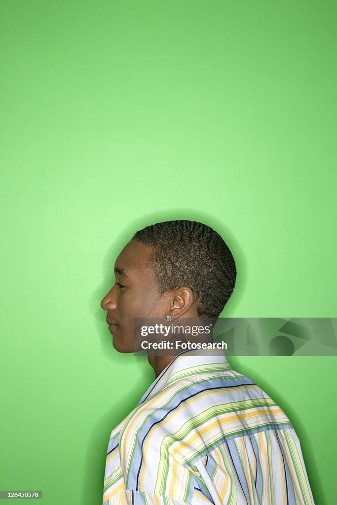 Side view portrait of African-American teen boy against green background.