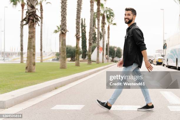 smiling young man walking on road against sky in city - walking side by side stock-fotos und bilder
