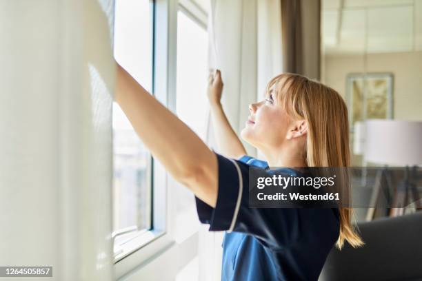 smiling chambermaid opening curtains of window in hotel room - curtain hotel stock-fotos und bilder