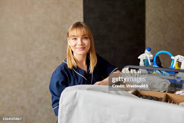 smiling chambermaid with push cart standing against wall in hotel corridor - reinier stockfoto's en -beelden