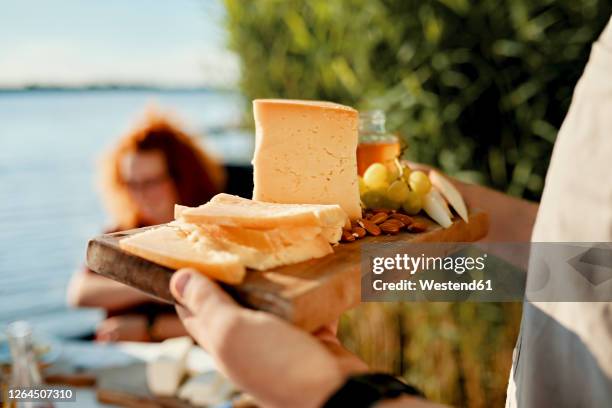 man serving cheese platter for friends at a lake - käseplatte stock-fotos und bilder