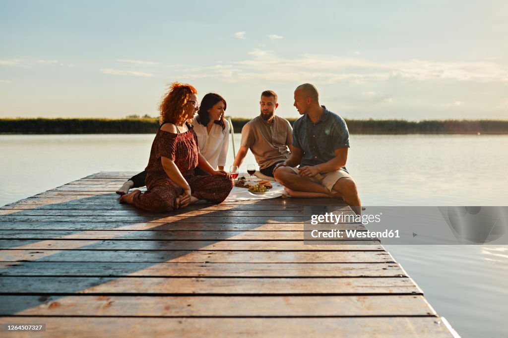 Friends having picnic on jetty at a lake at sunset