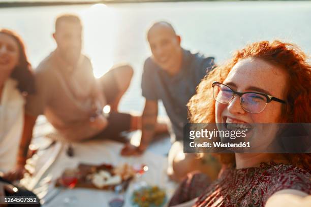 happy redheaded woman having picnic with friends on jetty at a lake at sunset - lake auburn stock pictures, royalty-free photos & images
