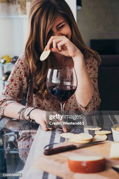 cheerful young woman holding cracker while sitting at dining table - covered food with wine stock pictures, royalty-free photos & images