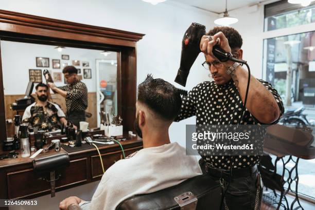 trendy hairdresser blow drying man's hair at salon - barbers stockfoto's en -beelden