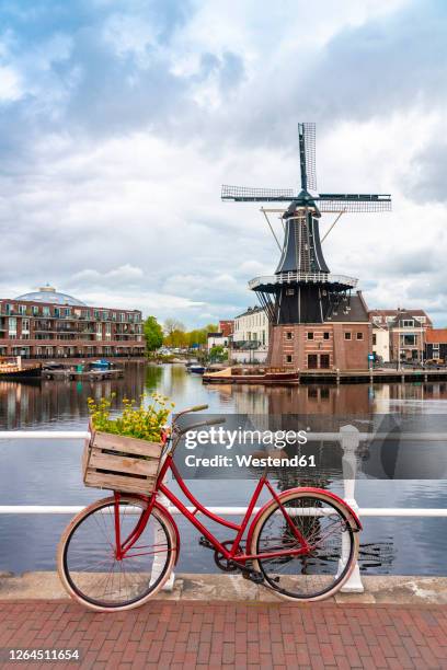 netherlands, north holland, haarlem, bicycle parked along railing of canal bridgewith de adriaan windmill in background - haarlem stock pictures, royalty-free photos & images