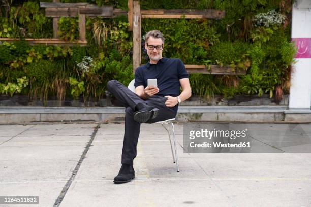mature man using smart phone while sitting on chair at yard - sitzen stock-fotos und bilder
