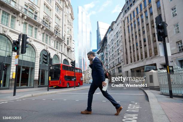 businessman talking on smart phone while crossing road in city - ein mann allein stock-fotos und bilder