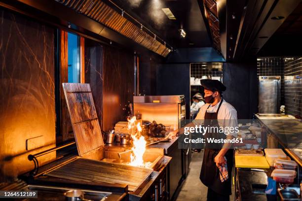 chef wearing protective face mask preparing grill in restaurant kitchen - in flames i the mask stock pictures, royalty-free photos & images