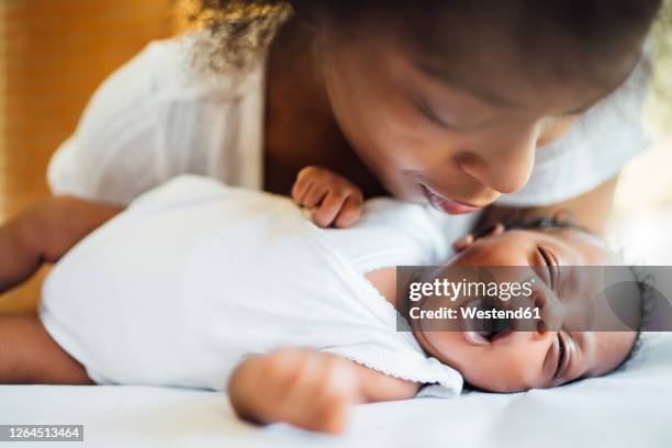 close-up of mother looking at cute newborn daughter yawning while lying on bed - baby close up bed stockfoto's en -beelden