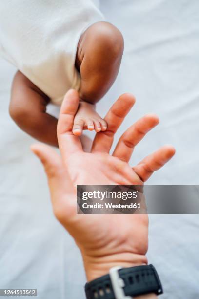 close-up of father hand touching newborn daughter's foot on bed - black men feet stock-fotos und bilder