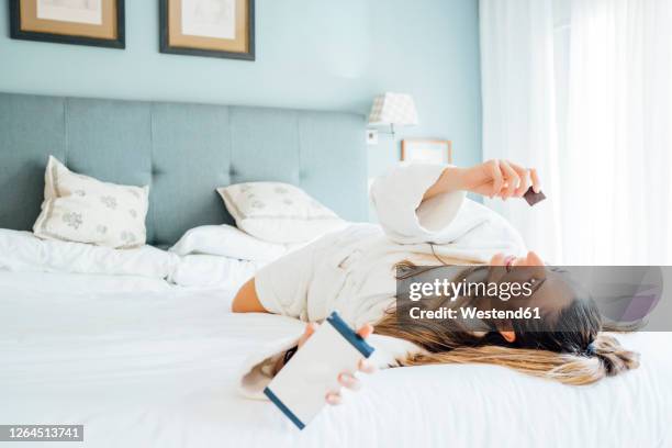 woman holding smart phone eating chocolate while lying on bed in hotel - chocolate happy stock pictures, royalty-free photos & images