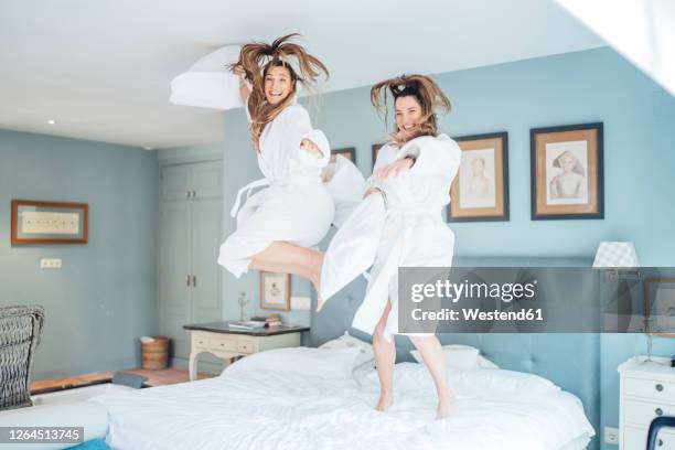 cheerful twin sisters jumping on bed in hotel room - zwilling stock-fotos und bilder
