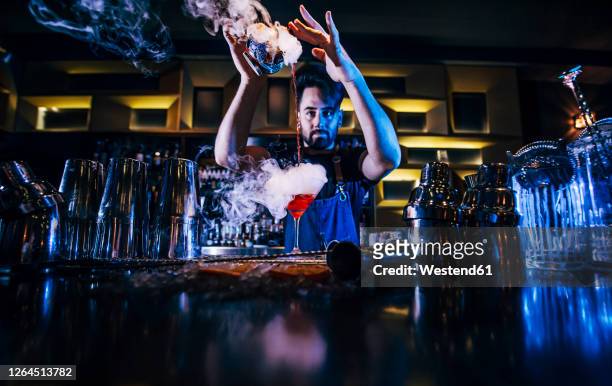 male bartender pouring cocktail in glass on bar counter at nightclub - cocktail counter stock-fotos und bilder
