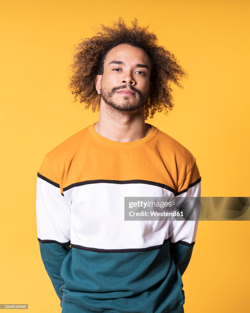 Handsome young man with curly hair standing against yellow background