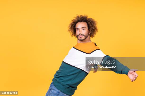 cool young man with curly hair dancing against yellow background - fashion man single casual shirt imagens e fotografias de stock