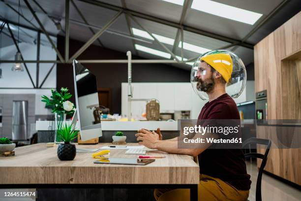 businessman wearing fishbowl while using computer at desk in modern office - new business covid stock pictures, royalty-free photos & images