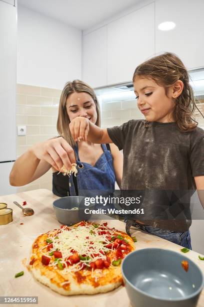 mother and daughter throwing cheese on pizza dough in kitchen - pizza toss stock-fotos und bilder