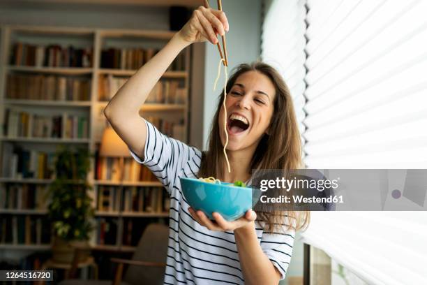 young woman eating spaghetti while sitting by window at home - consume photos et images de collection