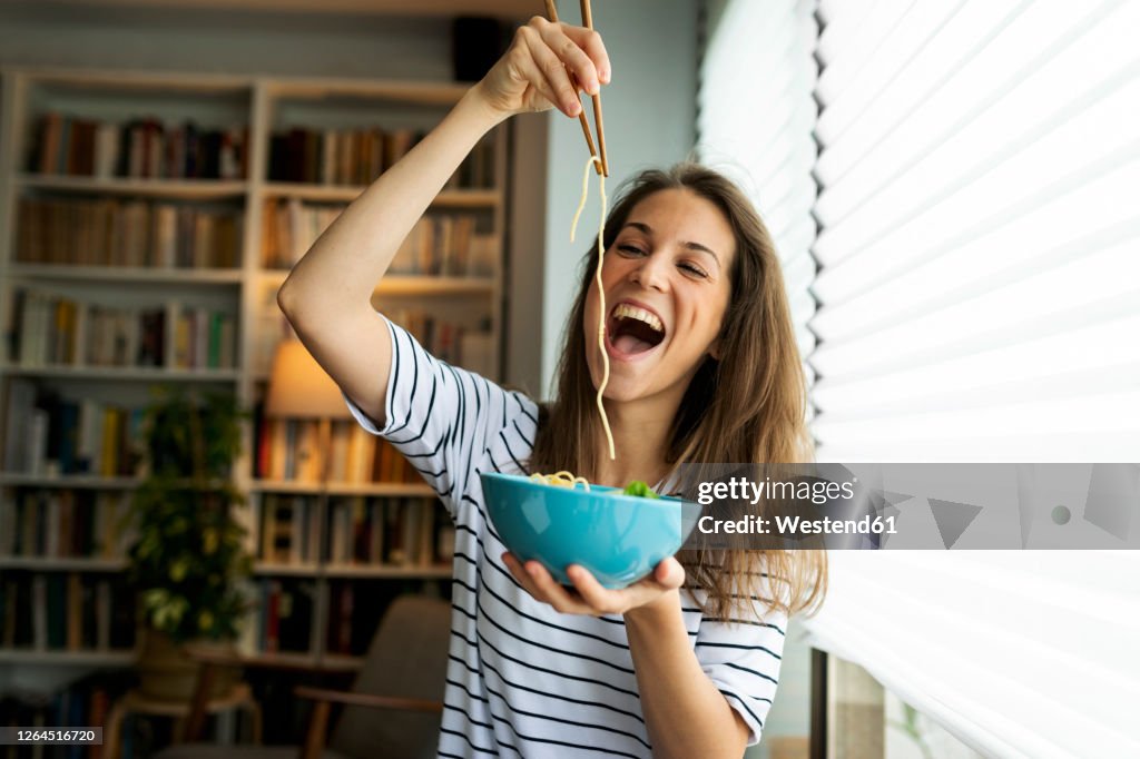 Young woman eating spaghetti while sitting by window at home